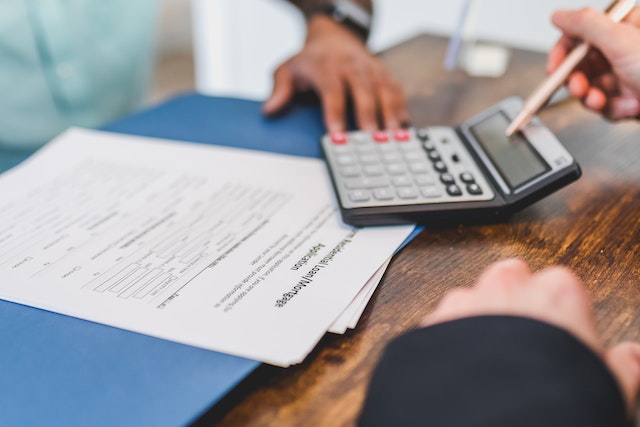 Close up of a desk where two people are looking at a document and a calculator